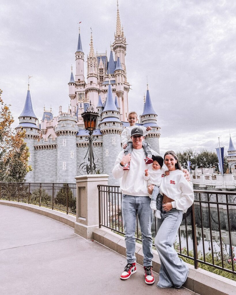 A family wearing matching white shirts poses in front of a large Disney castle.