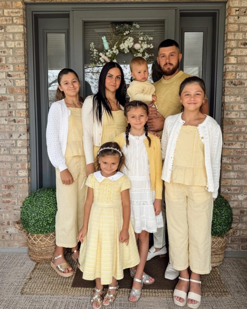 A family of seven wearing matching yellow and white patterned Easter outfits posing together.