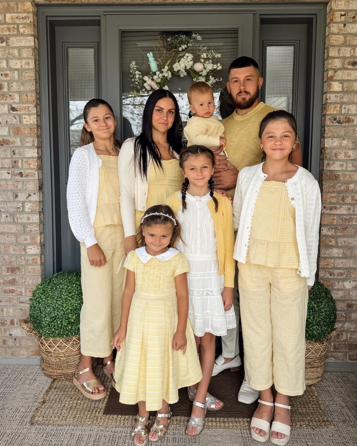 A family of seven wearing matching yellow and white patterned Easter outfits posing together.