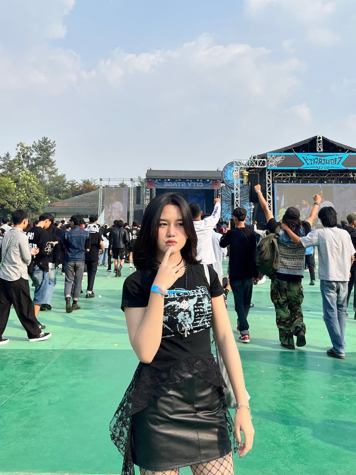 Young woman wearing a black graphic band tee and leather skirt at an outdoor music festival.