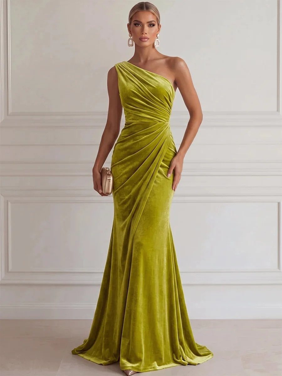 Woman in a floor-length olive green velvet one-shoulder dress posing against a white wall.