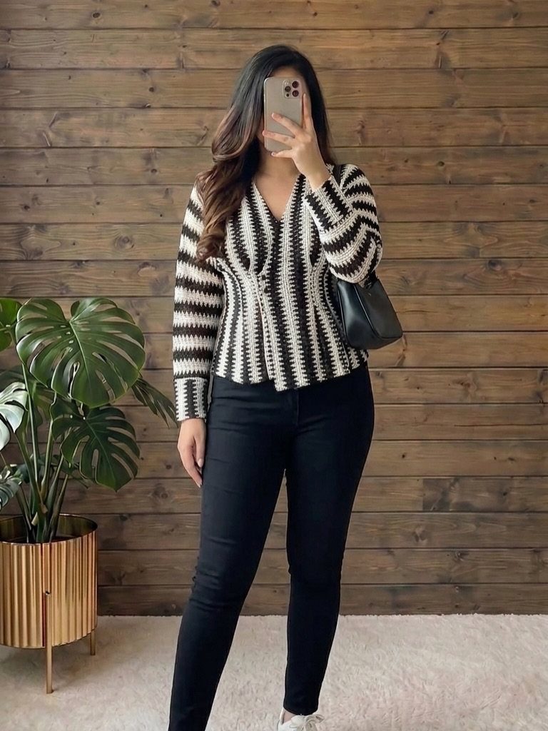 Woman wearing a striped black and white peplum top and black pants standing against a wooden wall.